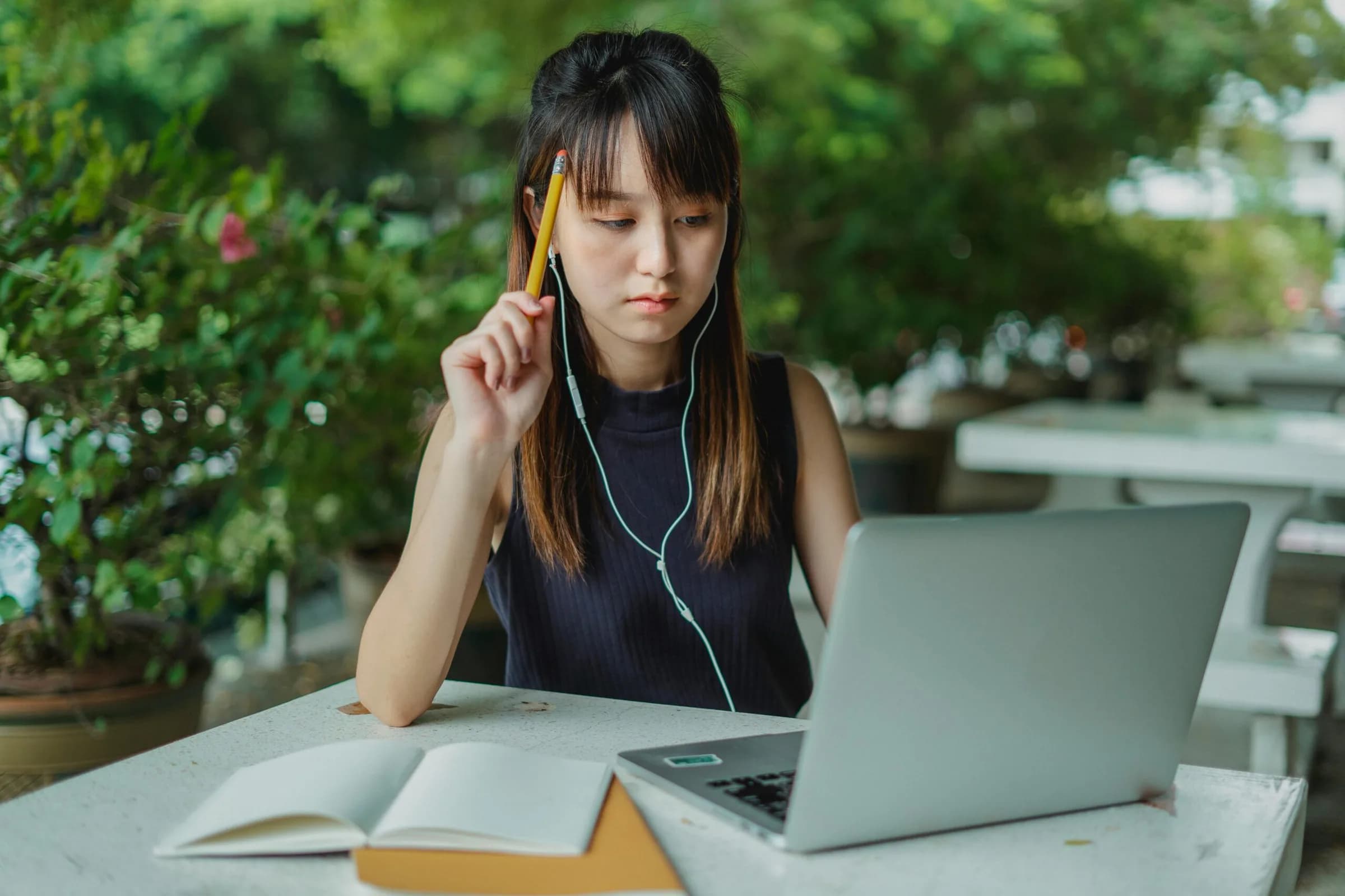 jeune femme, dans son jardin, devant son ordinateur, avec des écouteurs dans les oreilles, absorbée par ses cours en ligne