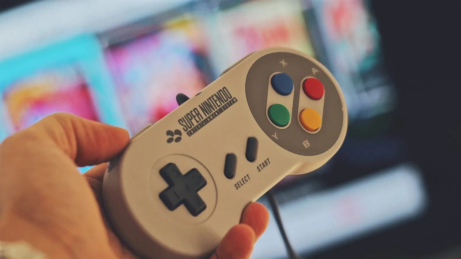 Main tenant un contrôleur de jeu classique Super Nintendo à l'intérieur avec un écran flou en arrière-plan.